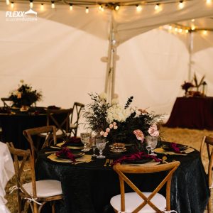 Table decorated in a jewel tone wedding palette with dark linens, gold place settings and flatware, and a floral centerpiece