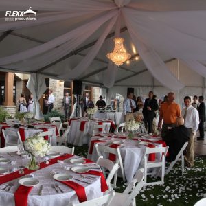 Wedding tent with chandelier, white ceiling drapery, and tables decorated in white and red linens in an old Hollywood style