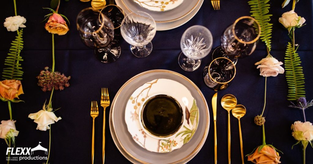 Wedding rentals including dark linen, china, flatware, and glassware placed on a table decorated with different flowers