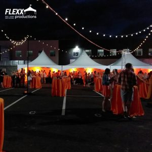 An outdoor event with orange linen highlights draped over tables and frame tents with orange ProColor uplighting