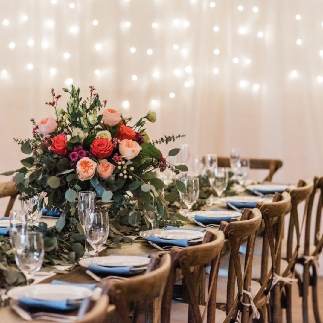 event-specialist-help-plan-wedding Napa wood table and chairs with gorgeous place settings, linens, a floral centerpiece, and fairy lights on a wall
