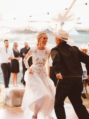 professional-tent-and wedding-rental-installation A smiling bride dancing with her dad on a dancefloor set up under a wedding tent rental with hanging market lights
