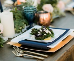 Gold flatware, gold charger, white dishware, and navy blue linen napkins make up a place setting at a wedding