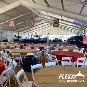 Tables, chairs, and linens set up under a large structure tent for an event
