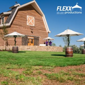 Beautiful white and bronze umbrellas, wine barrel tables, and other party rentals at an outdoor event
