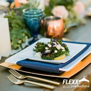 Square white china placed on gold chargers with blue linen napkins for a stylish holiday table setting