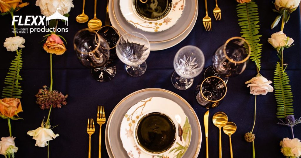 Stylish holiday table setting with glassware, china, chargers, and linens, complemented by decorative flowers