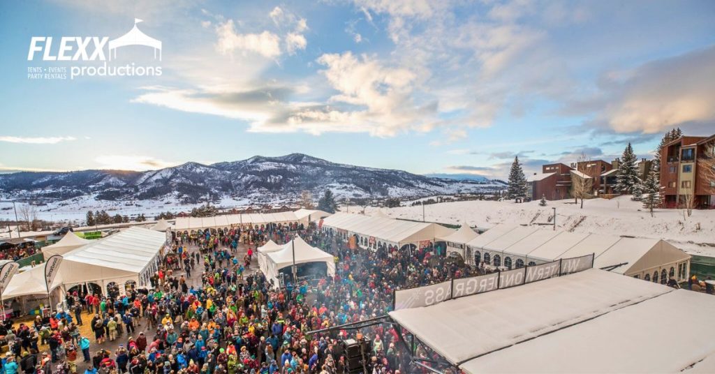 Winter festival in the mountains with multiple tents, stages, and a big crowd